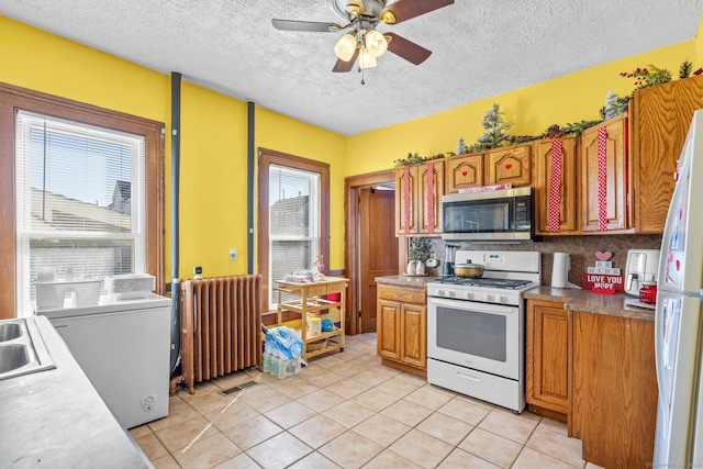 kitchen featuring white appliances, light tile patterned floors, radiator heating unit, ceiling fan, and a textured ceiling