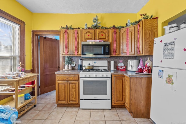 kitchen featuring white appliances, brown cabinetry, light tile patterned flooring, decorative backsplash, and a textured ceiling