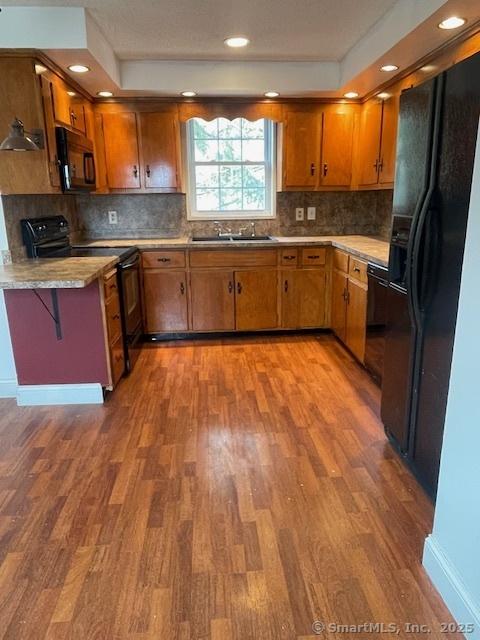 kitchen featuring brown cabinetry, wood finished floors, black appliances, and a sink