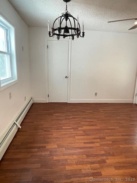 unfurnished dining area with baseboards, ceiling fan with notable chandelier, wood finished floors, a textured ceiling, and a baseboard radiator