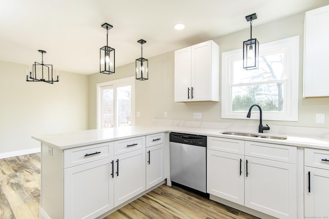 kitchen featuring dishwasher, a peninsula, light wood finished floors, and a sink