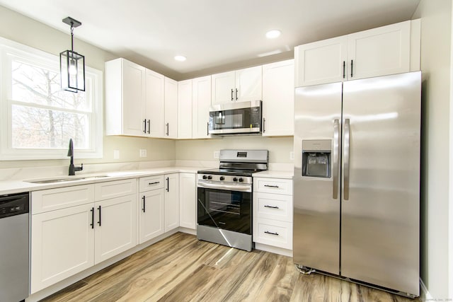 kitchen with light wood-type flooring, a sink, white cabinetry, stainless steel appliances, and light countertops