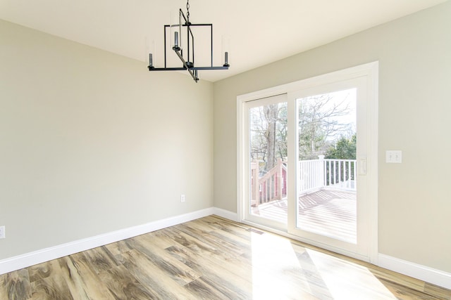 unfurnished dining area with baseboards, a notable chandelier, and light wood finished floors