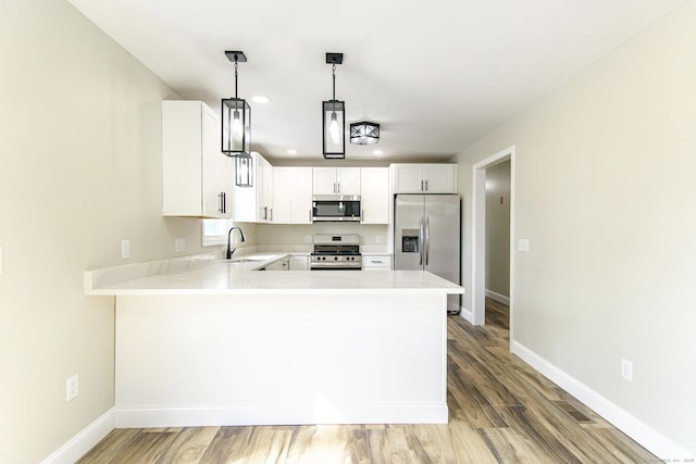 kitchen featuring stainless steel appliances, a peninsula, a sink, recessed lighting, and light countertops