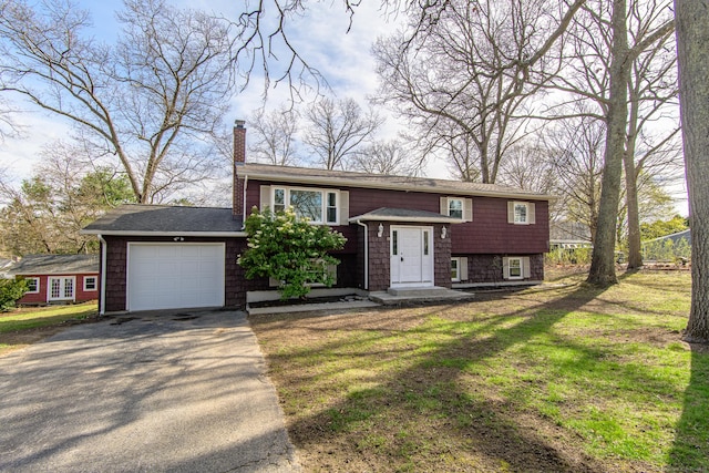 raised ranch featuring a garage, a chimney, aphalt driveway, a shingled roof, and a front yard