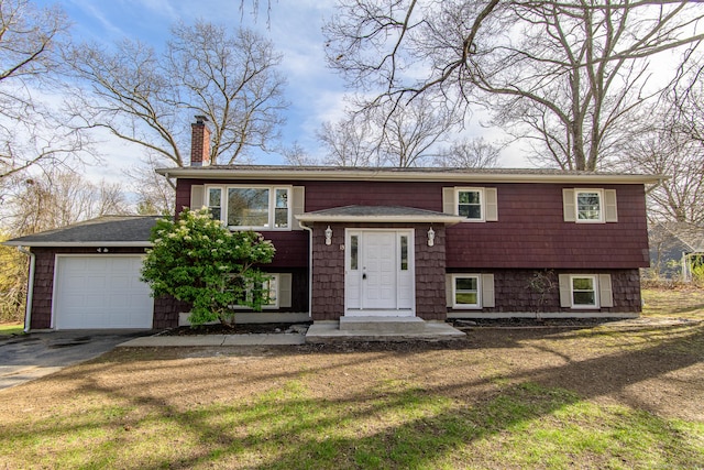 split foyer home with a front yard, an attached garage, driveway, and a chimney