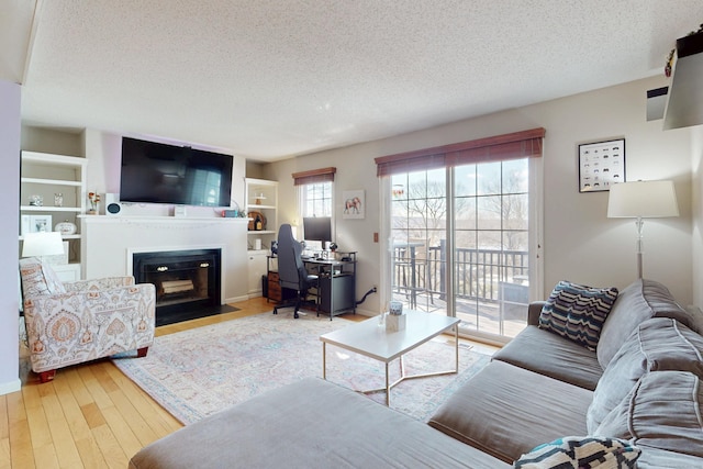 living room with a fireplace with flush hearth, built in features, a textured ceiling, and hardwood / wood-style floors