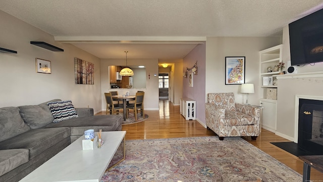 living room with a fireplace with flush hearth, a textured ceiling, baseboards, and wood finished floors