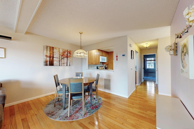 dining area with baseboards, visible vents, light wood finished floors, an inviting chandelier, and a textured ceiling