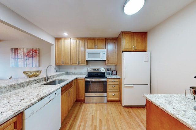 kitchen with light wood finished floors, white appliances, light stone counters, and a sink