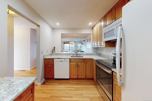 kitchen featuring a sink, white appliances, light wood-style floors, and light stone counters