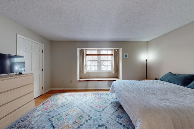 bedroom featuring visible vents, baseboards, a textured ceiling, and light wood-style flooring