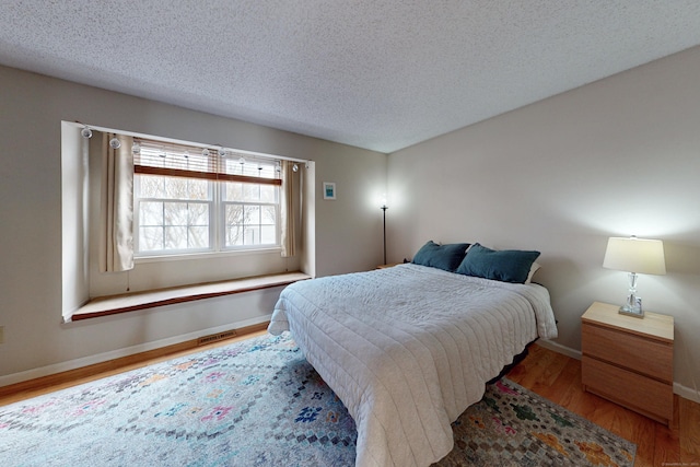 bedroom with baseboards, wood finished floors, visible vents, and a textured ceiling