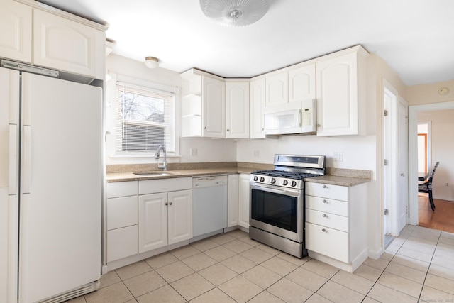 kitchen with a sink, white appliances, white cabinets, light tile patterned flooring, and light countertops