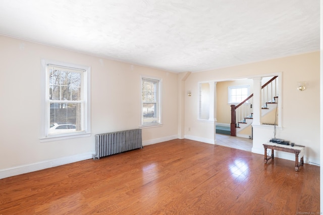 empty room featuring light wood-type flooring, baseboards, radiator, and stairway