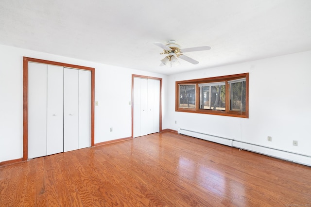 unfurnished bedroom with wood finished floors, two closets, ceiling fan, and a baseboard radiator