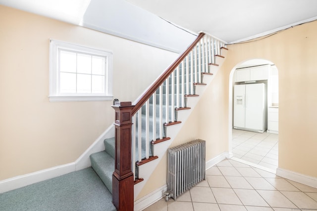 stairway with tile patterned floors, radiator heating unit, baseboards, and arched walkways