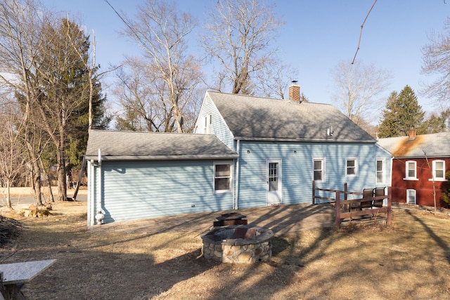 back of property with a fire pit, roof with shingles, and a chimney