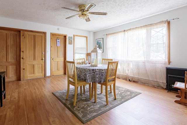 dining area with a ceiling fan, light wood-style floors, and a textured ceiling