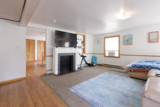 living area featuring a fireplace, cooling unit, a baseboard radiator, and wood finished floors