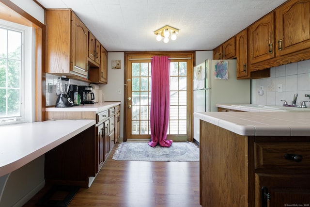 kitchen featuring a wealth of natural light, brown cabinetry, backsplash, and wood finished floors