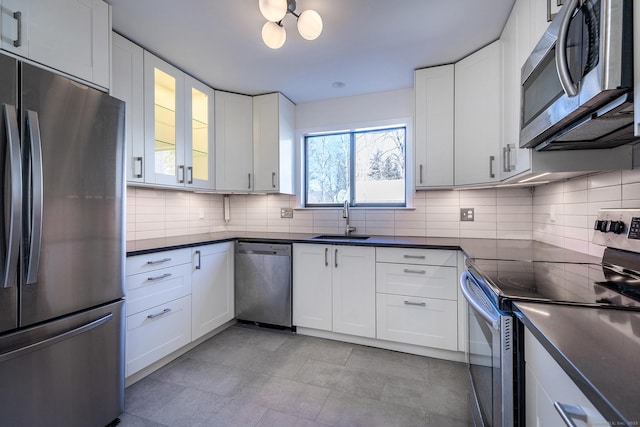 kitchen with dark countertops, tasteful backsplash, appliances with stainless steel finishes, white cabinets, and a sink