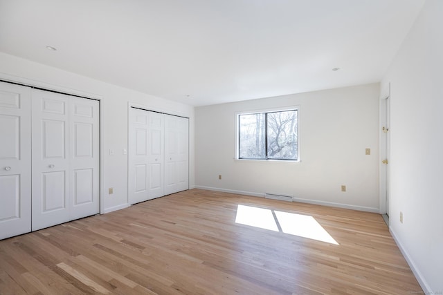 unfurnished bedroom with light wood finished floors, visible vents, two closets, and baseboards