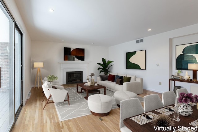 living area featuring a brick fireplace, light wood-style floors, visible vents, and baseboards