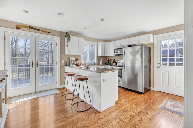 kitchen with light wood-style floors, a peninsula, appliances with stainless steel finishes, and white cabinets