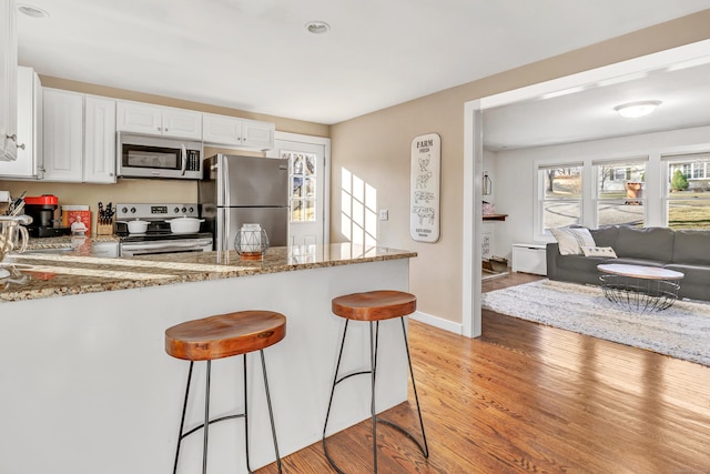 kitchen featuring a kitchen breakfast bar, open floor plan, white cabinetry, stainless steel appliances, and light wood finished floors