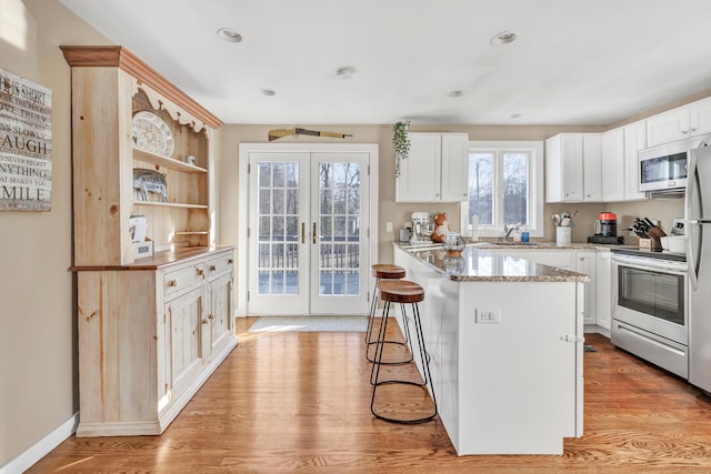 kitchen with a kitchen bar, light wood-style flooring, stainless steel range with electric cooktop, french doors, and a sink