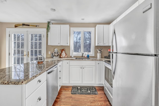 kitchen with a peninsula, a sink, stainless steel appliances, white cabinets, and french doors