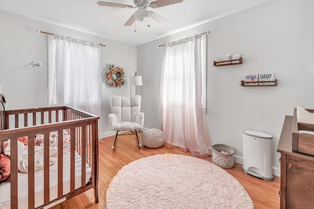 bedroom featuring baseboards, a nursery area, light wood-style flooring, and a ceiling fan