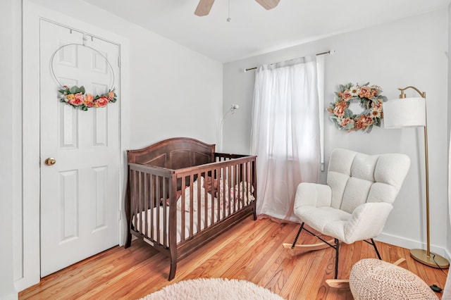 bedroom with a nursery area, a ceiling fan, light wood-type flooring, and baseboards