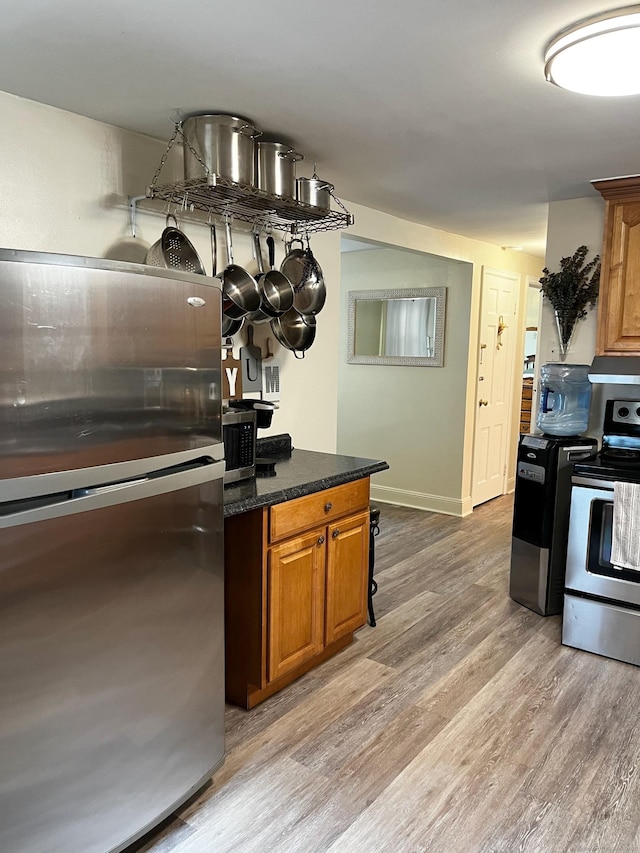 kitchen with light wood finished floors, baseboards, under cabinet range hood, brown cabinets, and appliances with stainless steel finishes