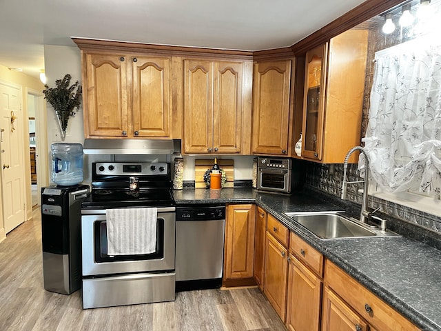 kitchen featuring light wood-style flooring, under cabinet range hood, a sink, appliances with stainless steel finishes, and glass insert cabinets