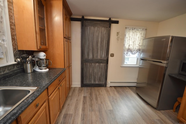 kitchen with light wood-type flooring, brown cabinets, glass insert cabinets, freestanding refrigerator, and a baseboard radiator