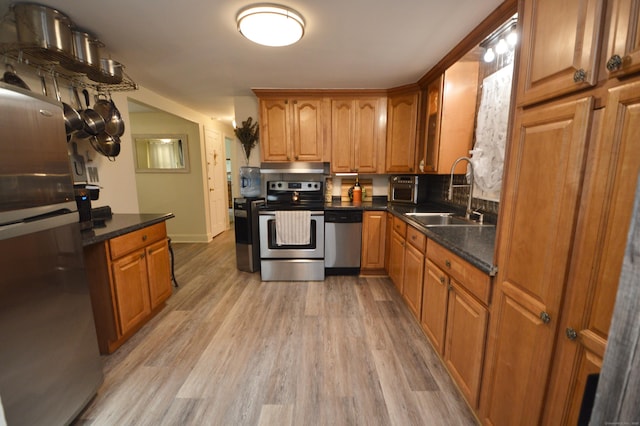 kitchen with brown cabinetry, light wood-type flooring, appliances with stainless steel finishes, and a sink