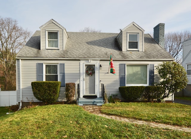 cape cod home with a shingled roof, a front yard, and fence