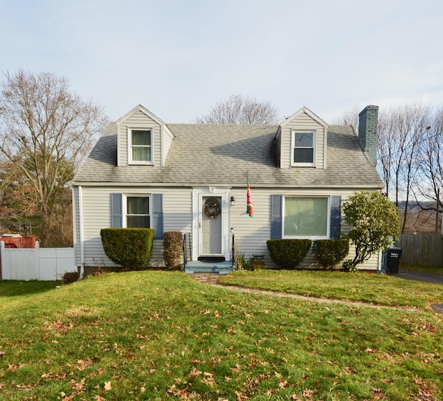 cape cod house with a front lawn, fence, a chimney, and a shingled roof