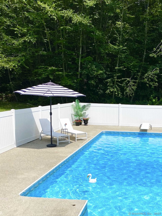 view of pool featuring a fenced in pool, fence, a patio area, and a diving board