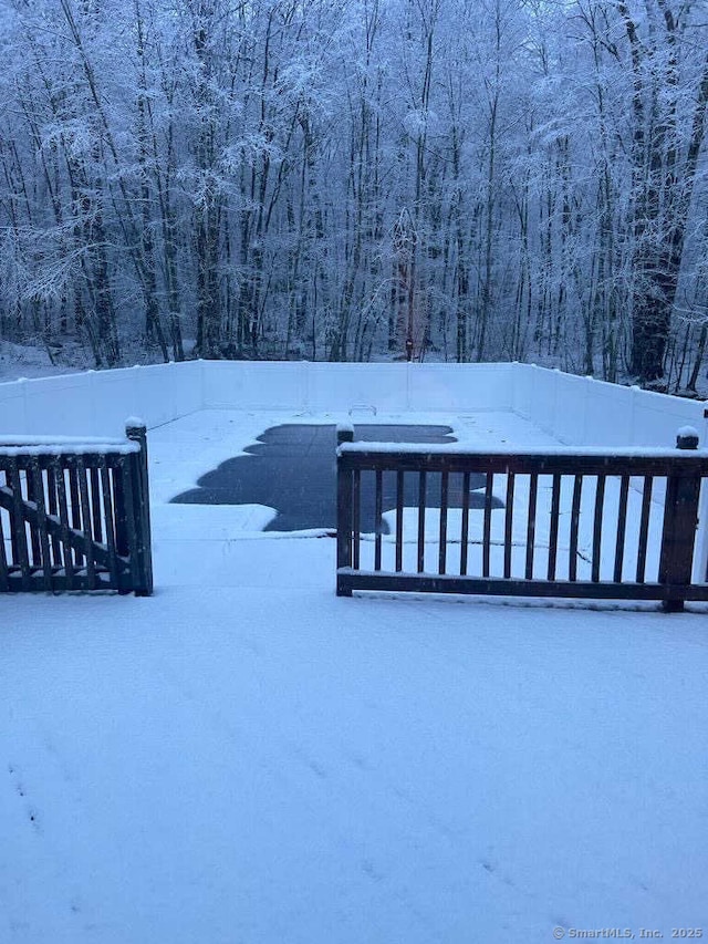 snow covered deck with fence and a wooded view