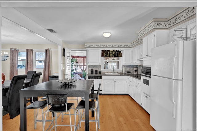 kitchen with a sink, dark countertops, white cabinetry, white appliances, and light wood finished floors