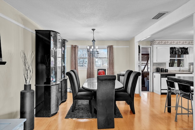 dining area with a textured ceiling, an inviting chandelier, visible vents, and light wood-type flooring