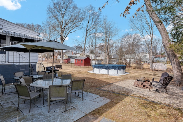 view of patio with outdoor dining space, fence, a covered pool, an outdoor structure, and a fire pit