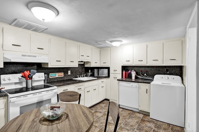 kitchen with white appliances, visible vents, washer / dryer, under cabinet range hood, and dark countertops