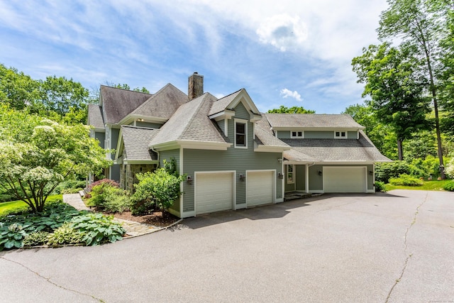 shingle-style home featuring aphalt driveway, an attached garage, a chimney, and roof with shingles