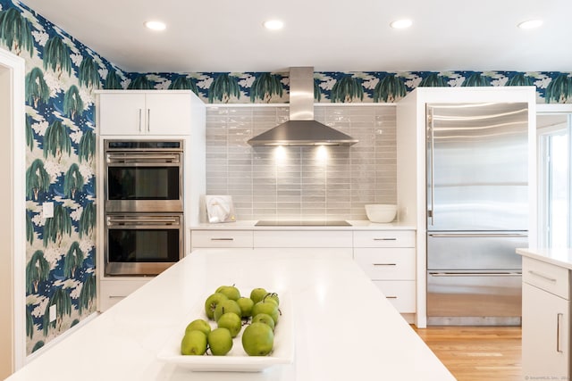 kitchen featuring wallpapered walls, stainless steel appliances, light countertops, white cabinets, and wall chimney range hood