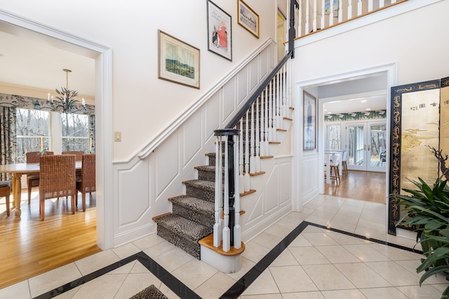 staircase with an inviting chandelier, a decorative wall, tile patterned floors, and a wealth of natural light