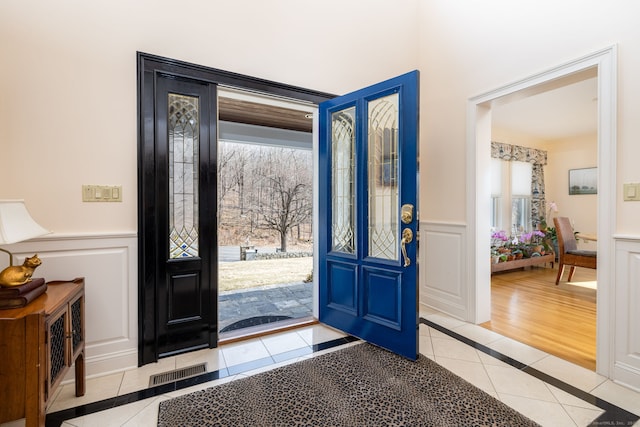 foyer entrance with a decorative wall, light tile patterned floors, visible vents, and wainscoting